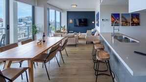 A modern living space with a dining area, kitchen, and large windows offering city views. - Zara Tower Hotel (Sydney)
