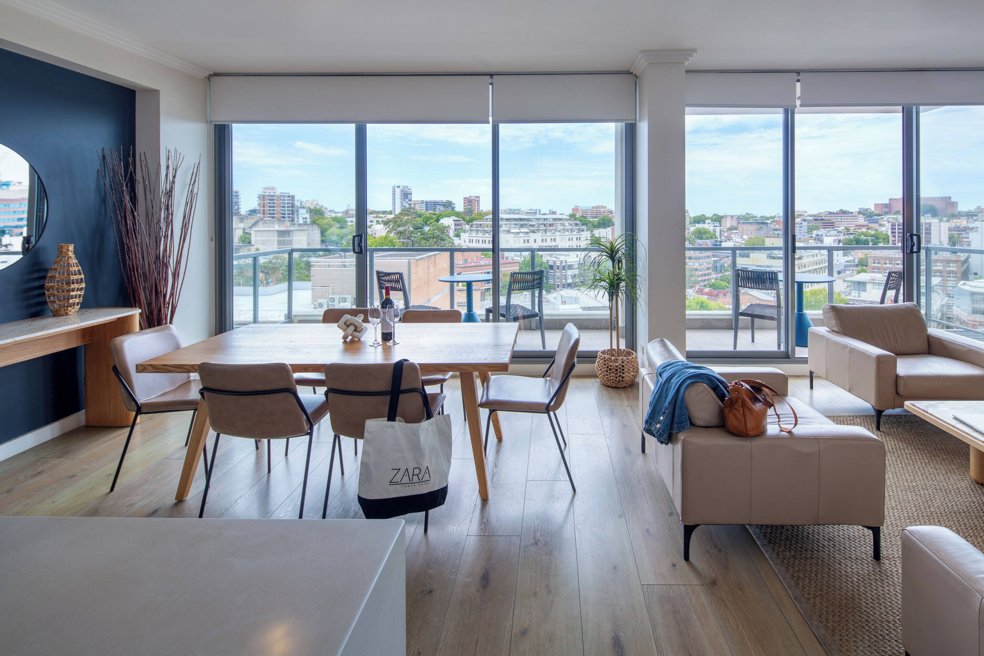 A modern living room with a dining area, large windows, and a city view.