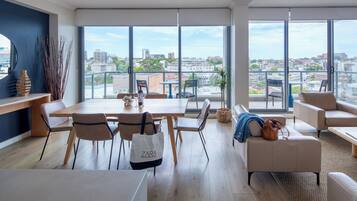 A modern living room with a dining area, large windows, and a city view.