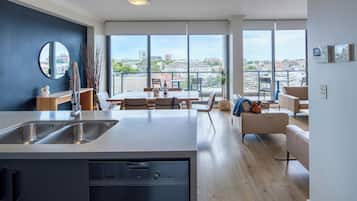 Una cocina moderna con lavavajillas, un comedor con mesa y sillas, y un amplio ventanal con vista a la ciudad.