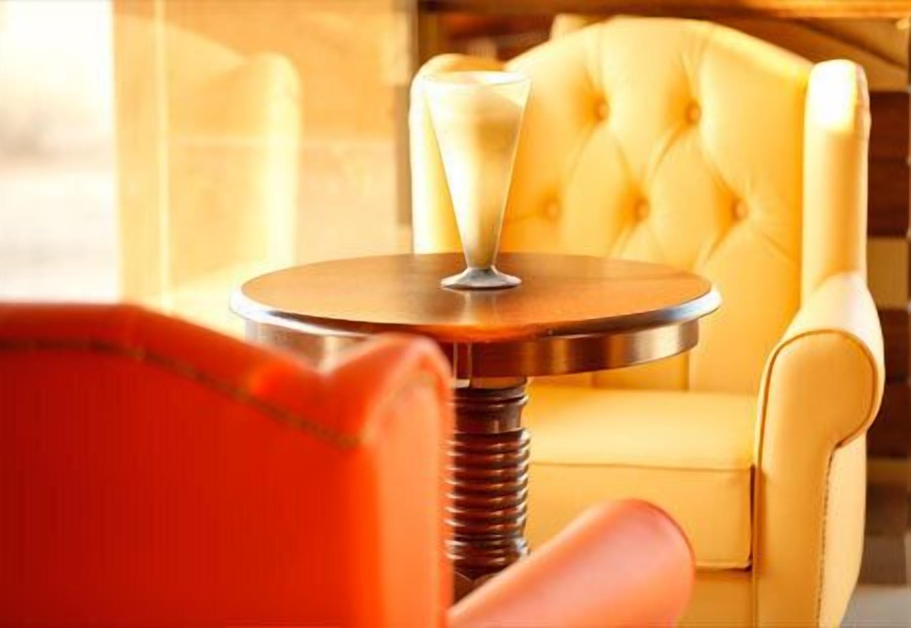 Een ronde tafel met een metalen voet, geplaatst voor een geel bekleden fauteuil.