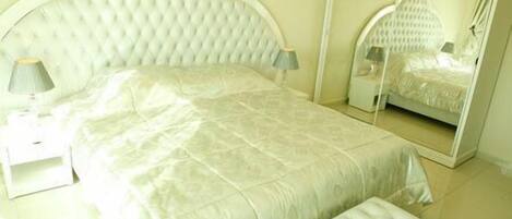 A bedroom with a bed, a nightstand, a lamp, a mirror, and a bench.