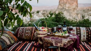 A picnic setup with a basket of fruits, cheese, and wine on a patterned blanket, overlooking a mountainous landscape. - Ortahisar Cave Hotel (Ürgüp)