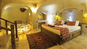 A bedroom with a large bed, a bathtub, and a wooden staircase. - Ortahisar Cave Hotel (Ürgüp)