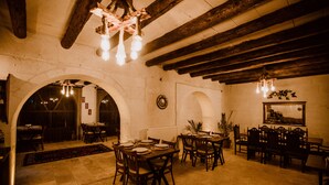 A dining area with wooden tables and chairs, a chandelier, and a rustic ceiling. - Ortahisar Cave Hotel (Ürgüp)