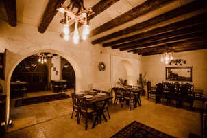 A dining area with wooden tables and chairs, a chandelier, and a rustic ceiling.
