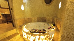 A circular hot tub with a tray of snacks and a bottle of wine, surrounded by stone walls and a wooden bench. - Ortahisar Cave Hotel (Ürgüp)