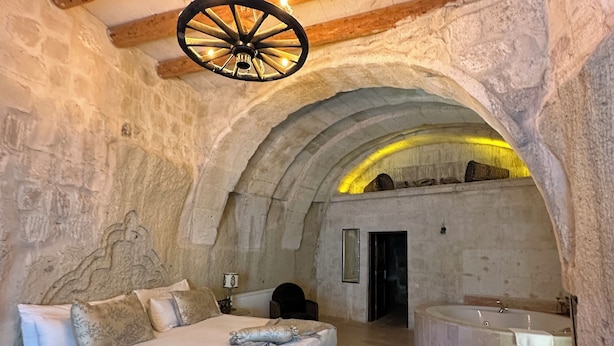A stone-walled bedroom with a bed, a small table, and a bathtub. - Ortahisar Cave Hotel (Ürgüp)