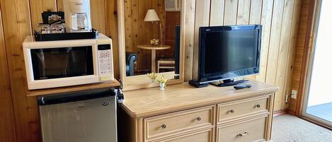 Una kitchenette compacta equipada con microondas, refrigerador y una pequeña mesa con lámpara.