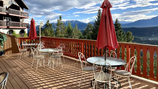 Um deck de madeira com mobiliário externo, guarda-corpo vermelho e vista para as montanhas.