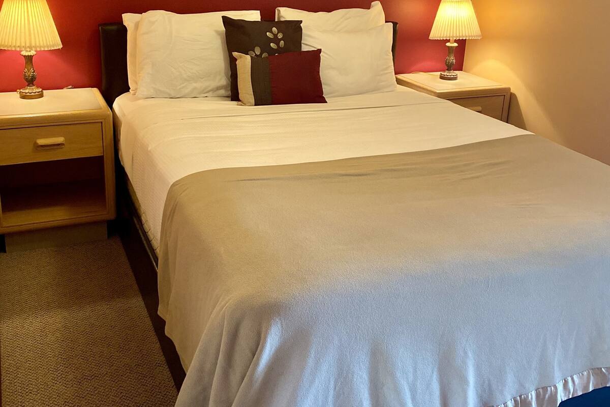 Een hotelkamer met een groot bed, twee nachtkastjes met lampen, een lijst met kunst aan de muur, en een rode accentmuur.