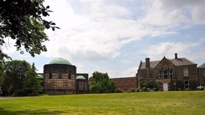 A large building with a green dome and a brick structure, surrounded by a grassy field and trees. - The Mirfield Monastery (Mirfield)