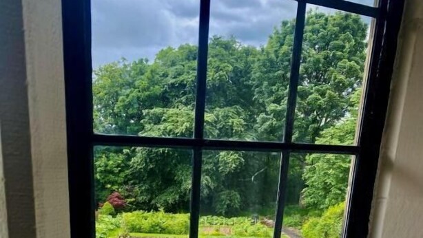 A window with a view of a lush garden with various plants and a greenhouse. - The Mirfield Monastery (Mirfield)