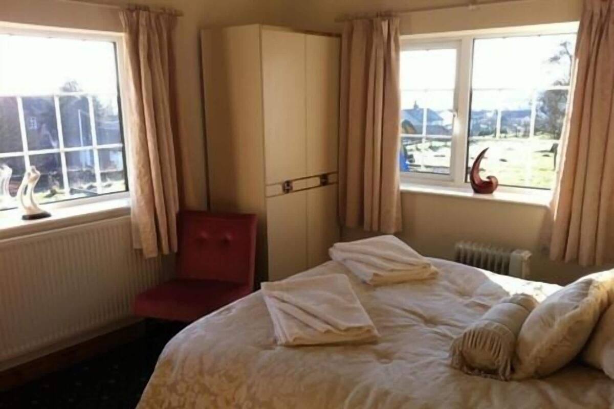 A hotel room with a bed, a red chair, a wardrobe, and a window with curtains.