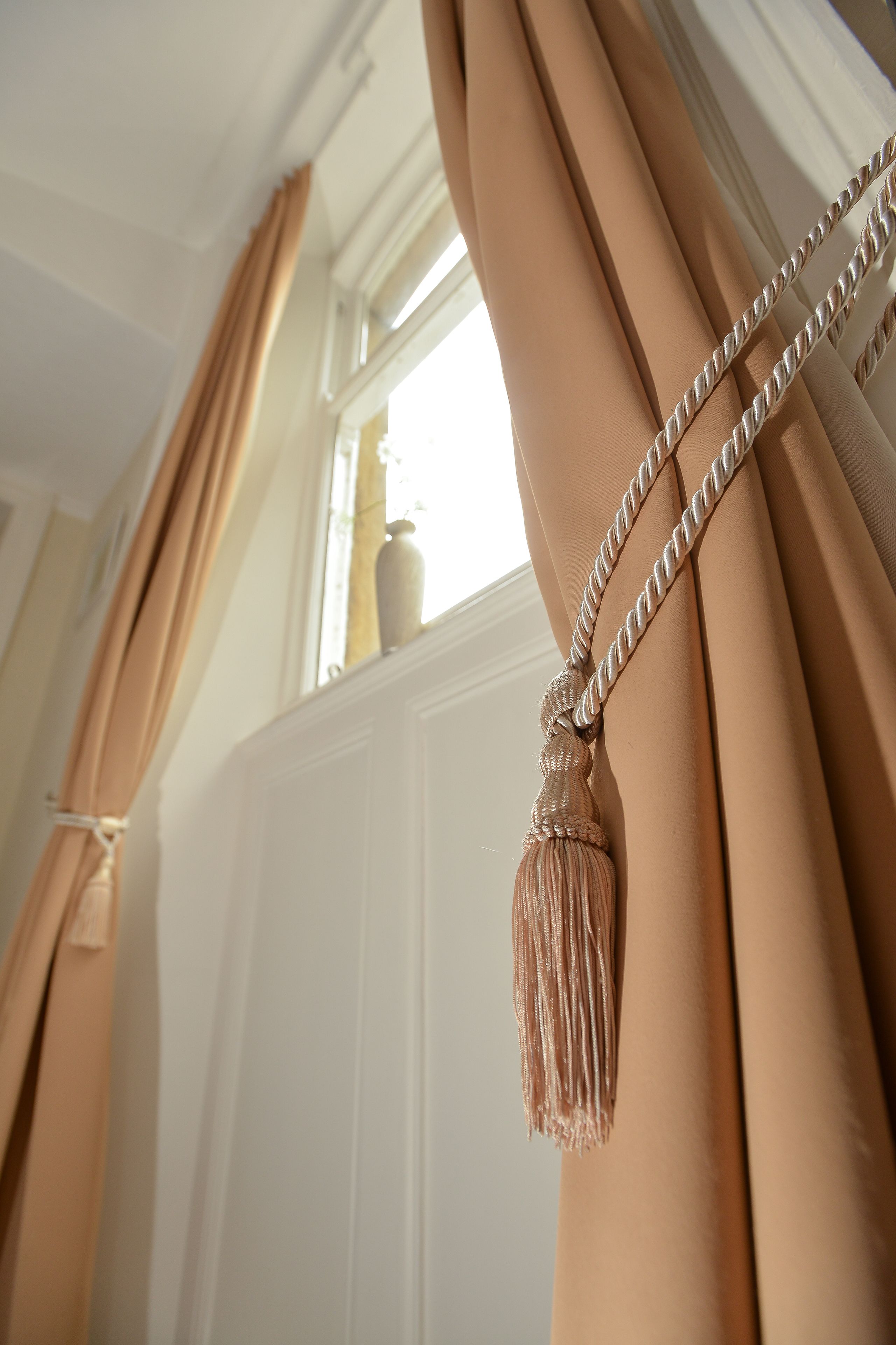 A close-up of curtains with a tassel, a window, and a radiator.