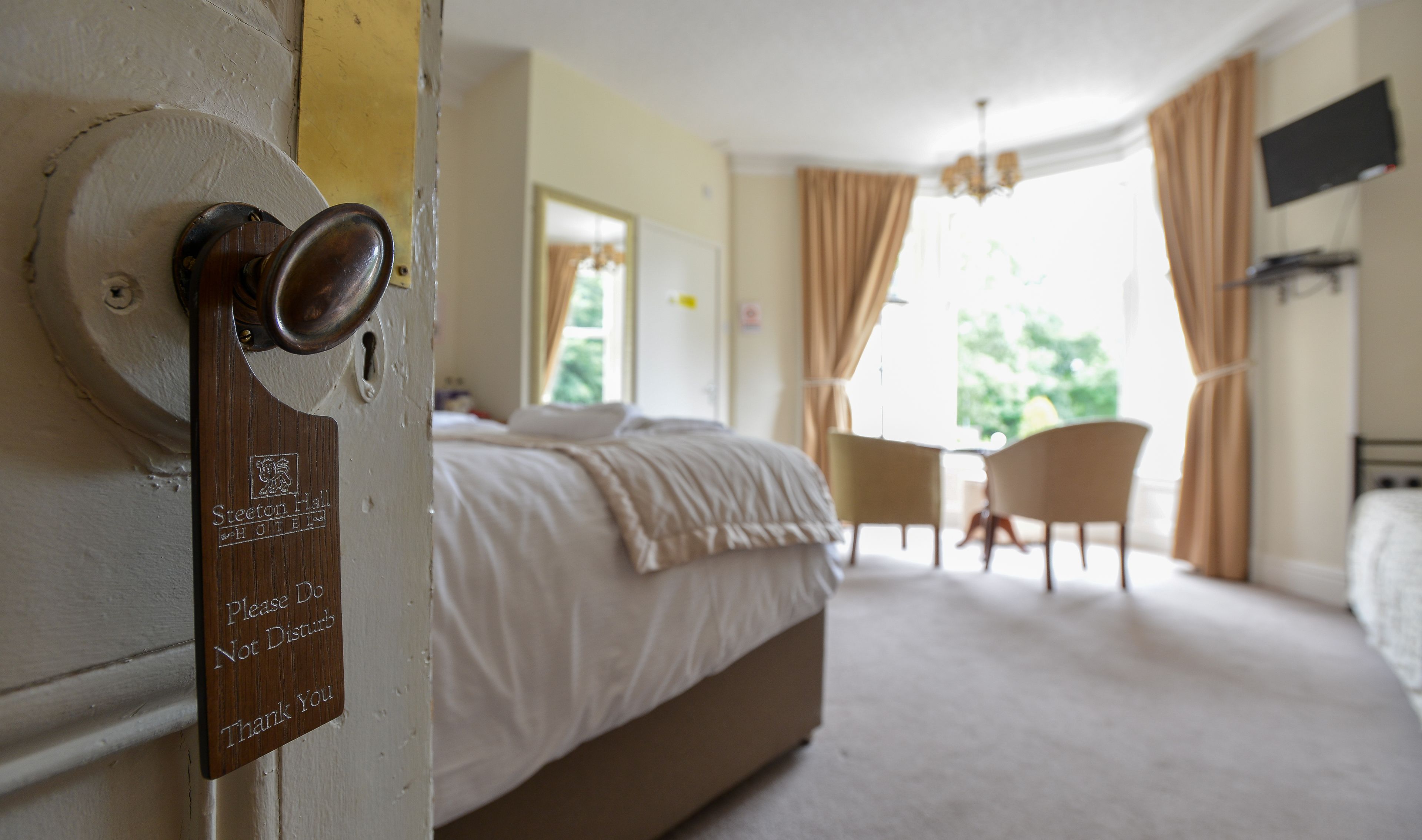 A hotel room with a bed, a desk, and a chair. There is a door with a sign that says "Please Do Not Disturb Thank You".