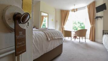 A hotel room with a bed, a desk, and a chair. There is a door with a sign that says "Please Do Not Disturb Thank You".