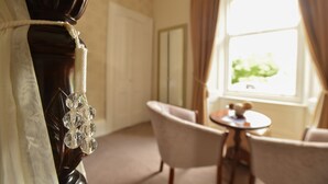 A room with a wooden chair, a small round table, and a window with curtains. - Steeton Hall Hotel (Keighley)