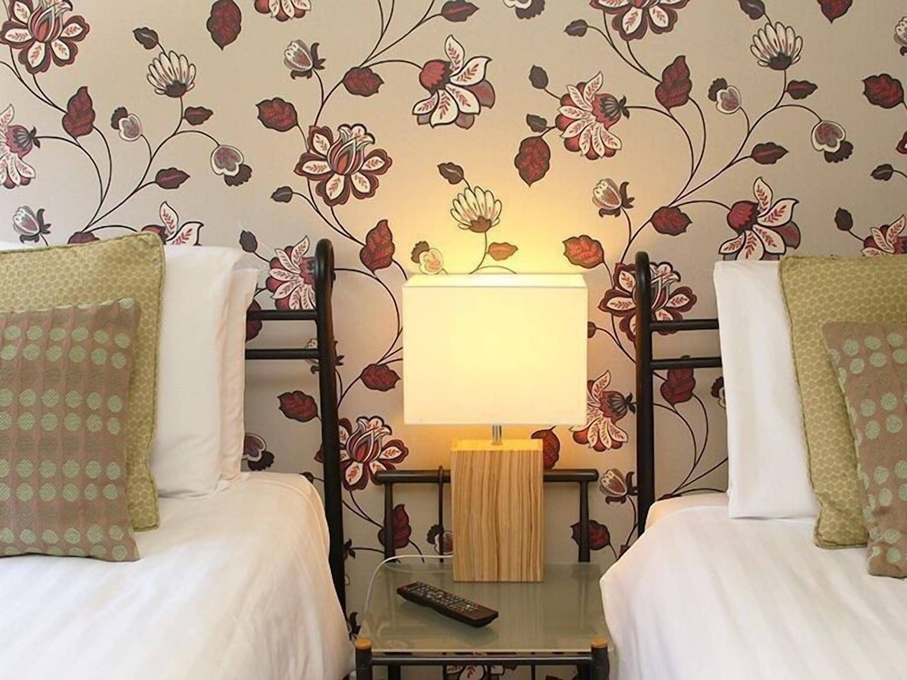Quarto de hotel com duas camas, uma mesa de cabeceira com abajur e um controle remoto sobre a mesa.