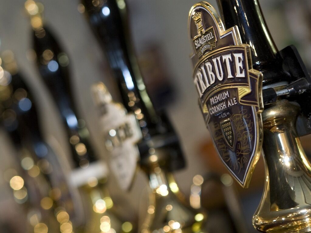 A close-up of a beer tap labeled "Tribute Premium Cornish Ale" with a gold and black design.