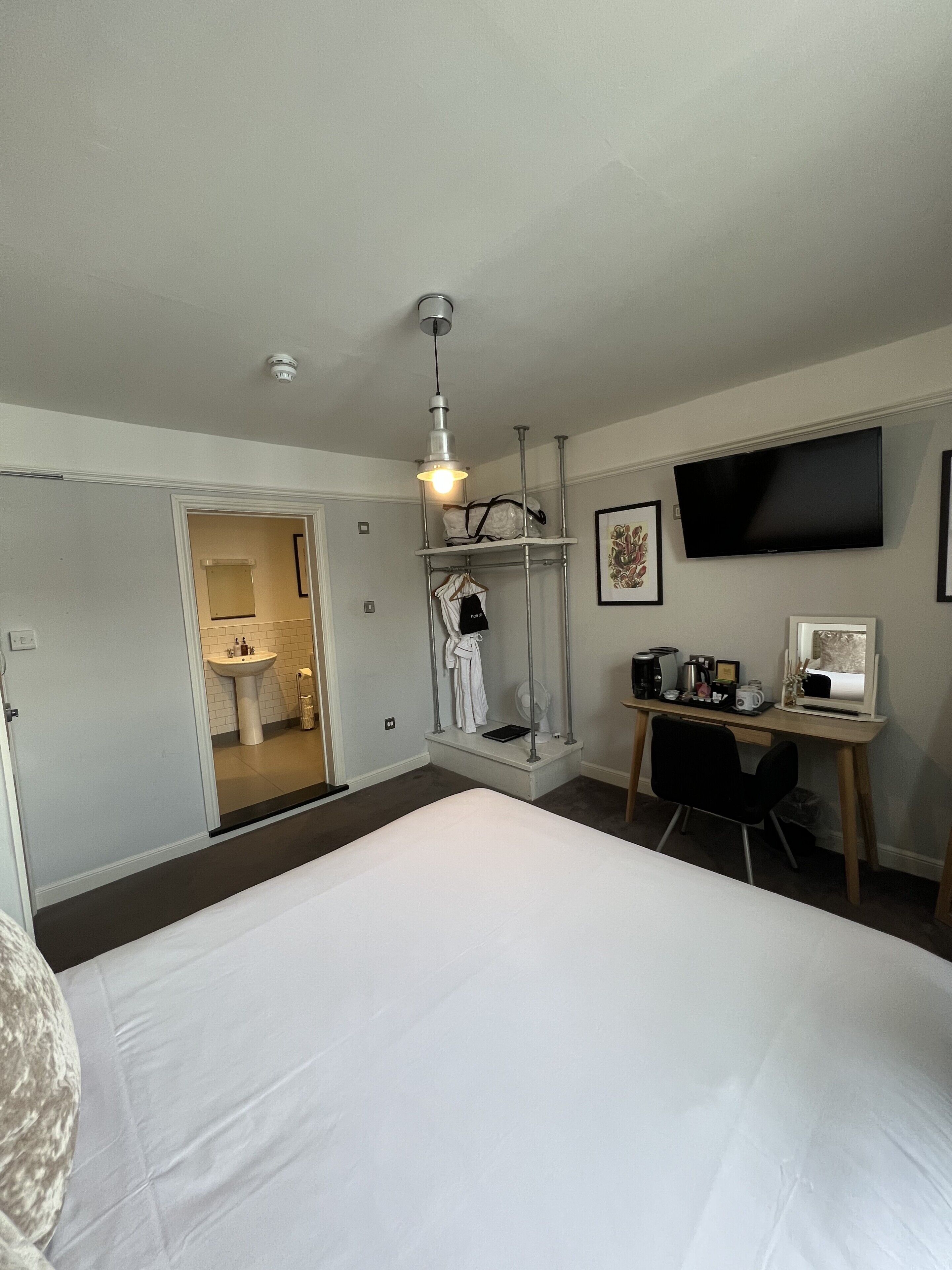 Quarto de hotel com uma cama grande, uma escrivaninha com computador, televisão e chuveiro.