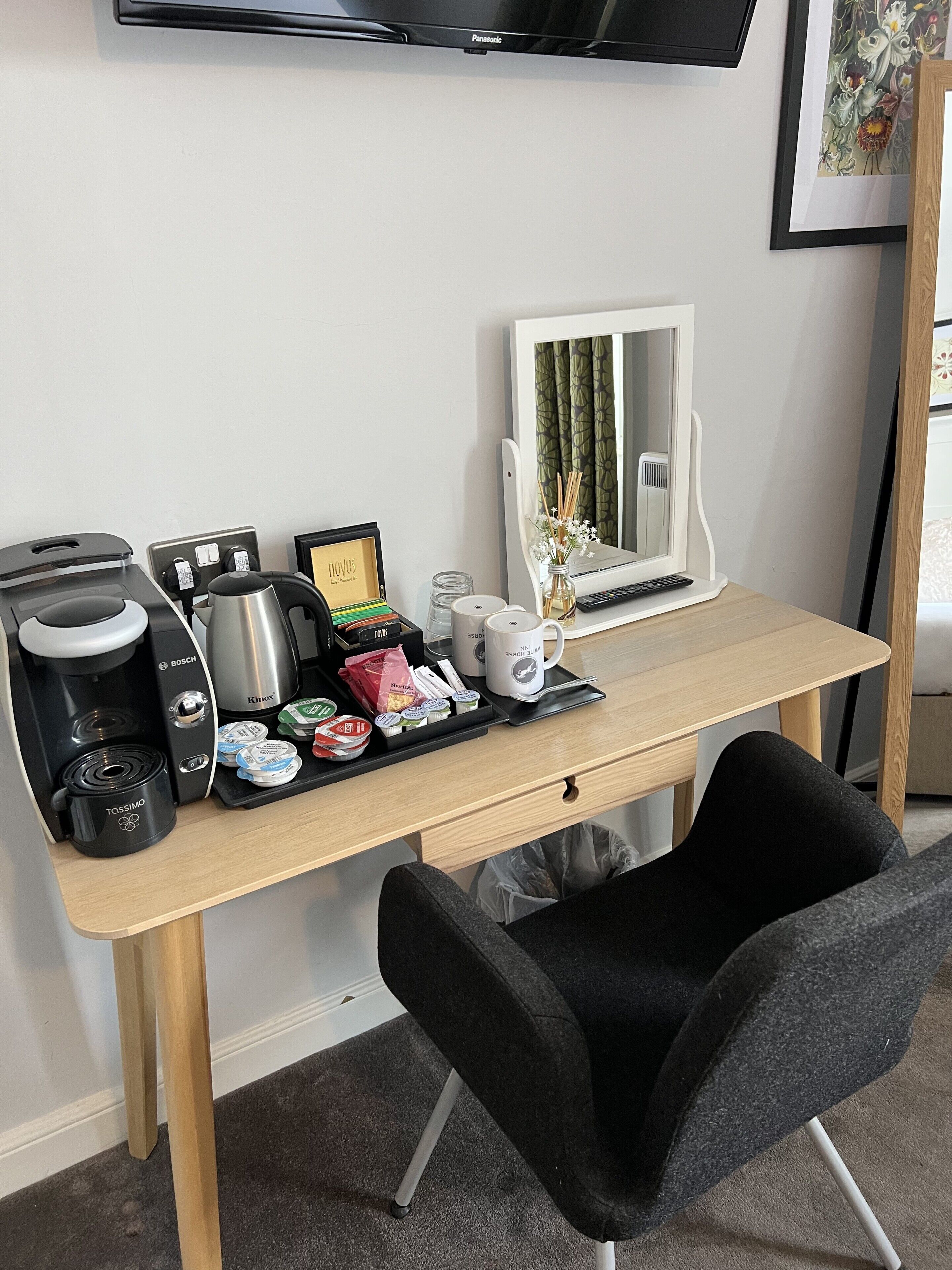 A neatly organized workspace with a coffee maker, a computer, a mirror, and a small plant.