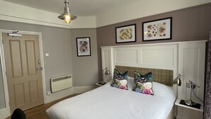 A bedroom with a bed, a nightstand, a chair, a ceiling fan, and framed artwork on the wall. - The White Horse (Maldon)
