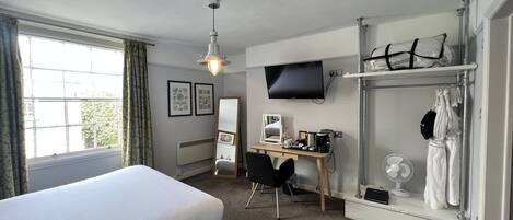Habitación de hotel con cama, escritorio, silla, televisor y vestidor.