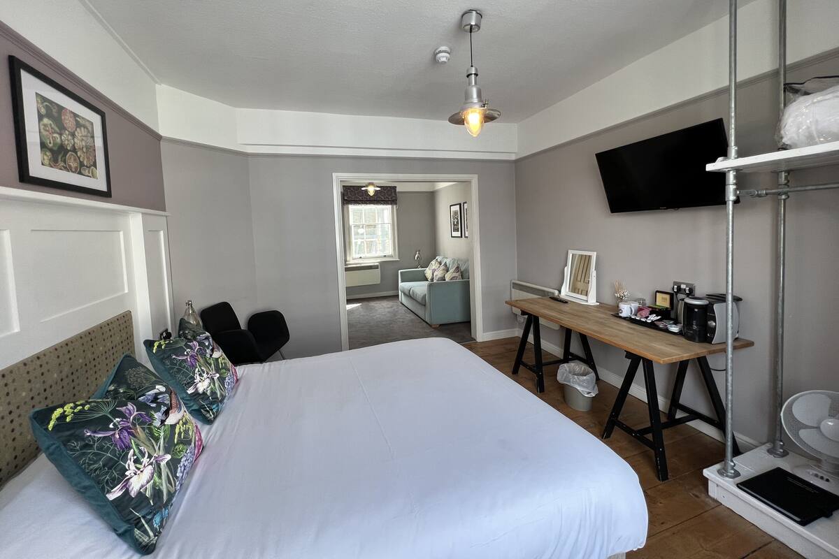A hotel room with a bed, a desk, a TV, and a shower area.