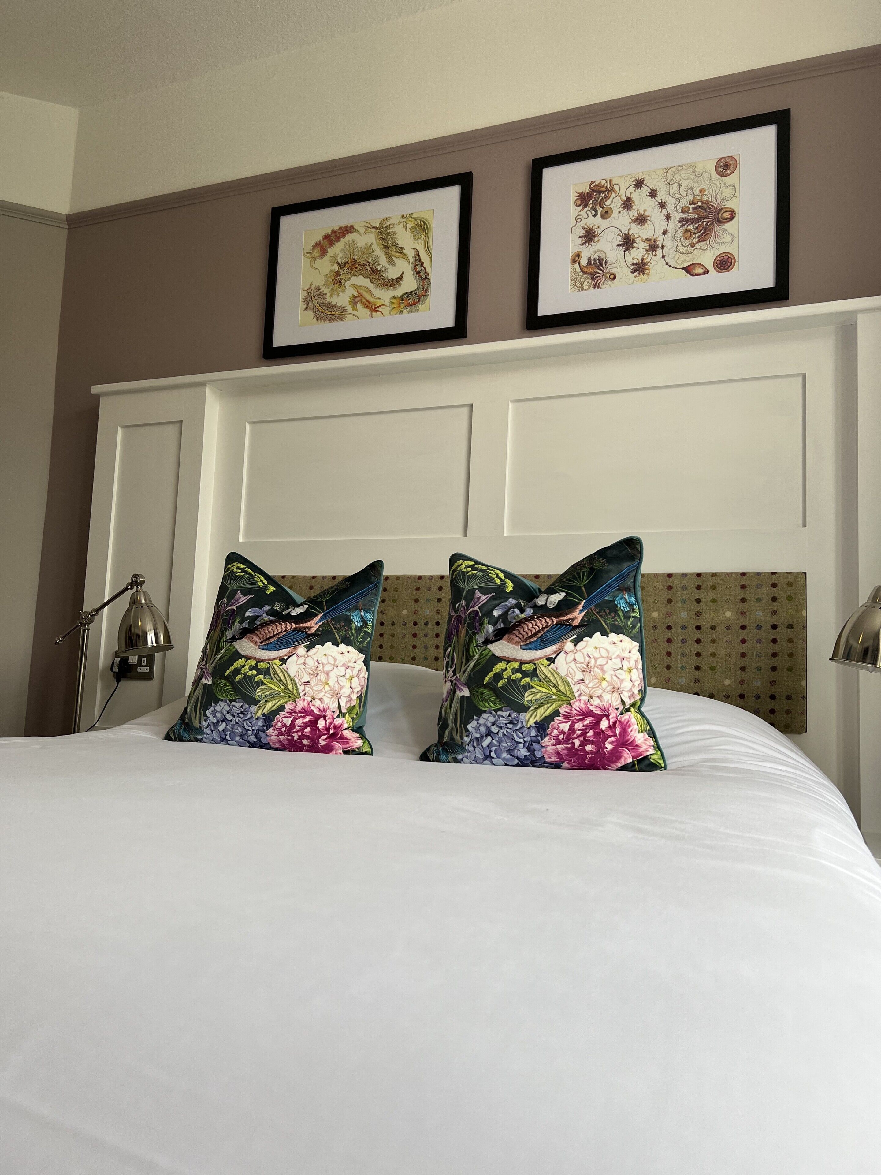 Una cama con almohadones florales, un cabecero blanco y dos cuadros enmarcados encima.