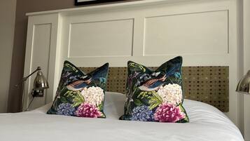 Una cama con almohadones florales, un cabecero blanco y dos cuadros enmarcados encima.