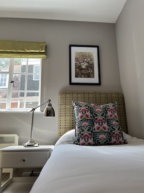 Un dormitorio con cama, mesita de noche, lámpara, ventana con vistas a edificios y un cuadro en la pared.