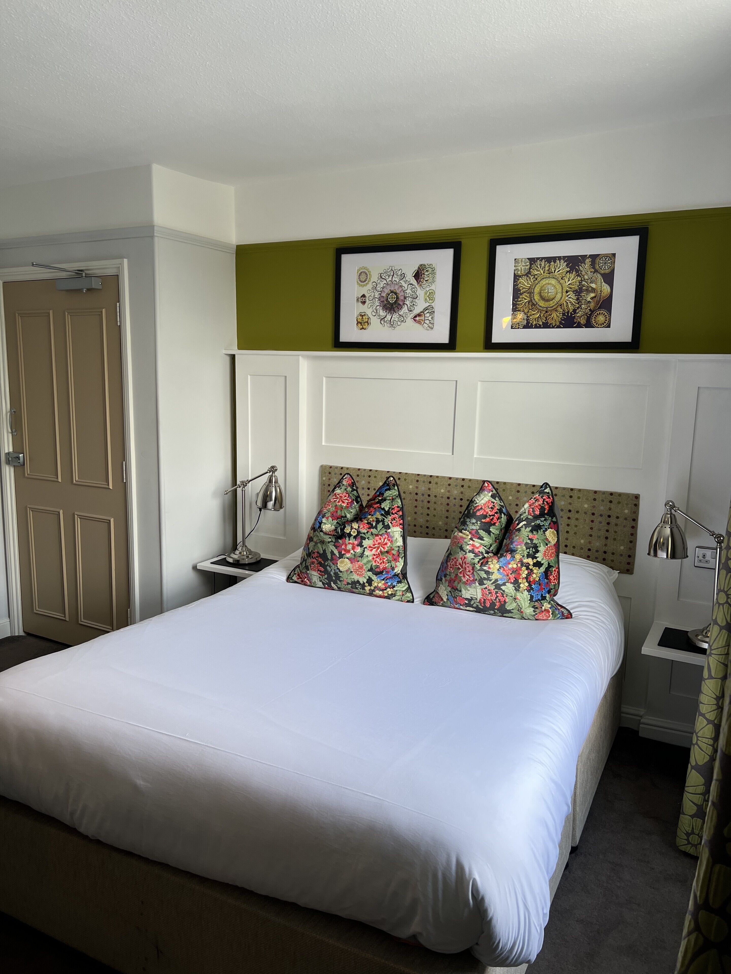 A neatly made bed with floral pillows, a framed picture above it, and a door to the left.