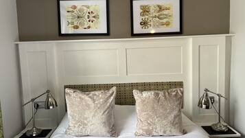 Una cama bien hecha con dos almohadas, cabecera con panel decorativo, dos lámparas de noche y dos obras de arte enmarcadas en la pared.