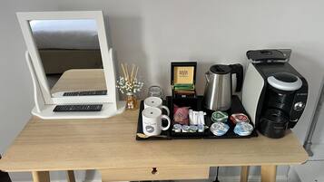 A desk with a computer monitor, keyboard, coffee maker, and various coffee pods.