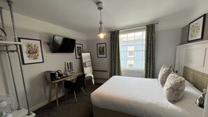 Ein Hotelzimmer mit Bett, Schreibtisch mit Stuhl, einem an der Wand befestigten Fernseher und einem Fenster mit Vorhängen.