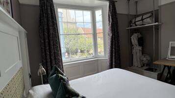 Un dormitorio con una cama grande, una ventana con cortinas, una mesita de noche con lámpara y un perchero con bata.
