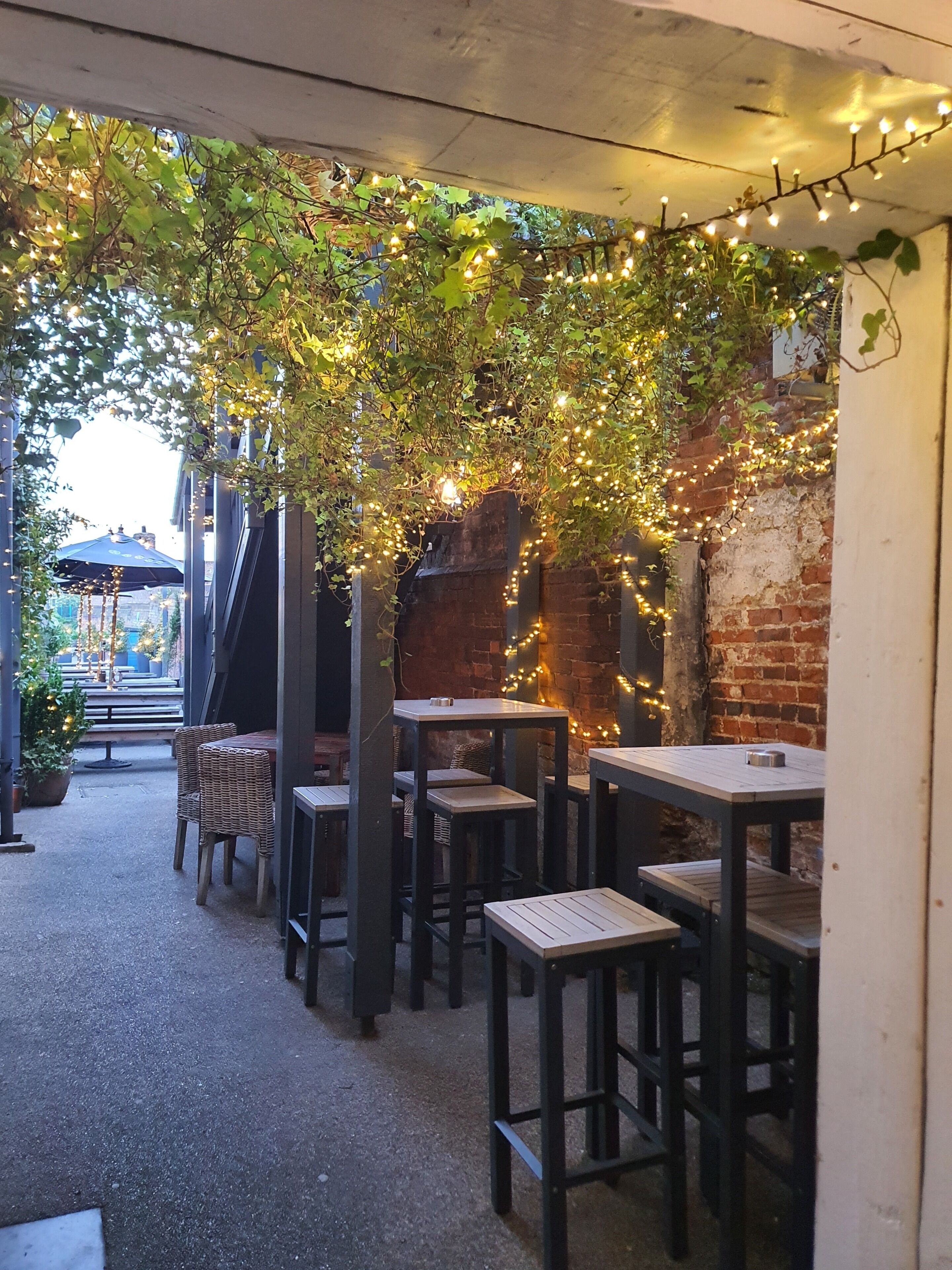 An outdoor seating area with tables and chairs, string lights, and greenery.