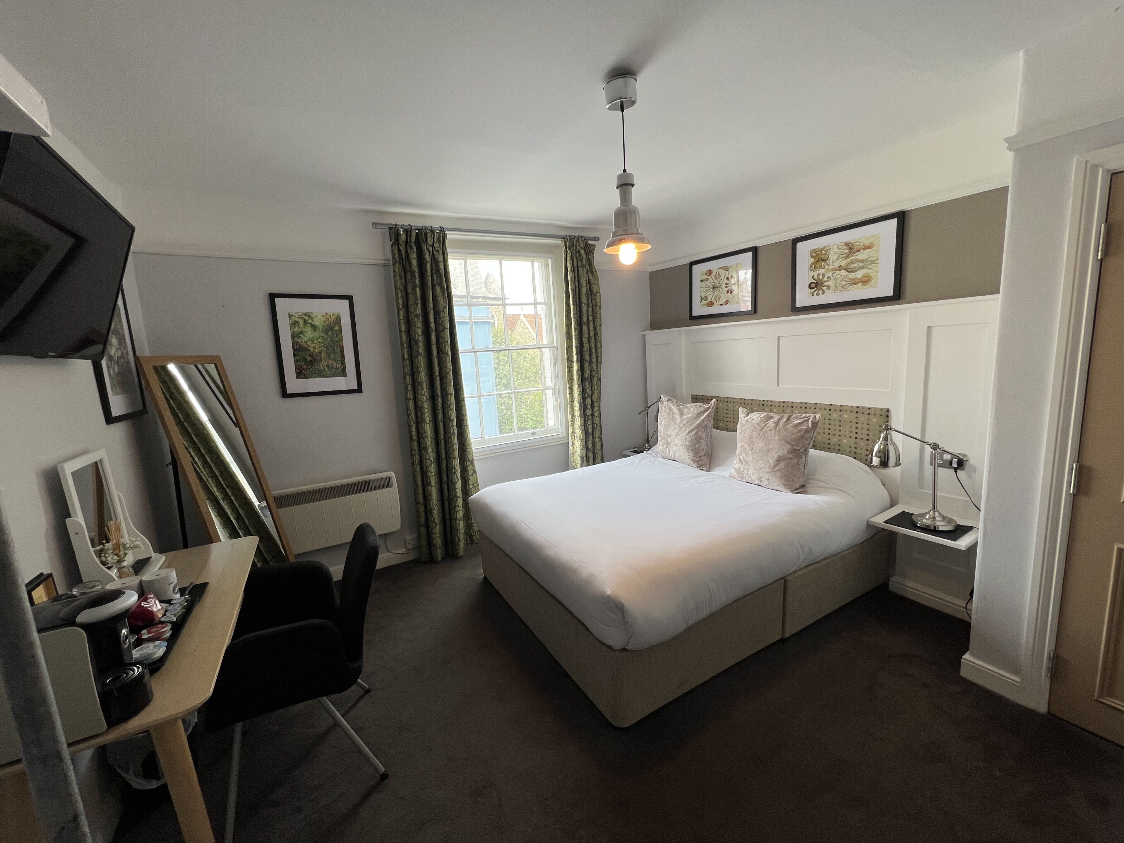 A bedroom with a bed, bedside table, lamp, chair, desk, and a window with curtains.