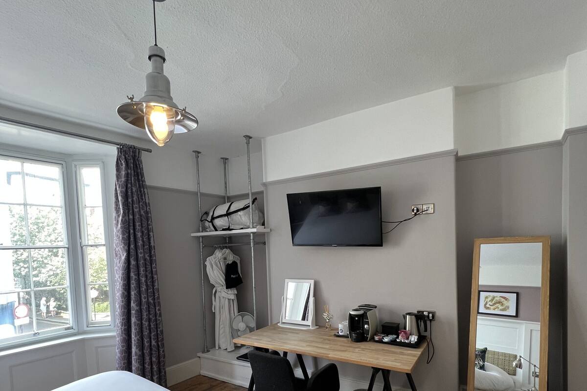 A bedroom with a bed, wooden floor, a desk with a computer, a TV, and a mirror.