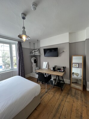 A bedroom with a bed, wooden floor, a desk with a computer, a TV, and a mirror. - The White Horse (Maldon)