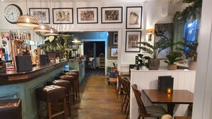 Eine Bar mit Hockern, einer Theke und gerahmten Kunstwerken an den Wänden.