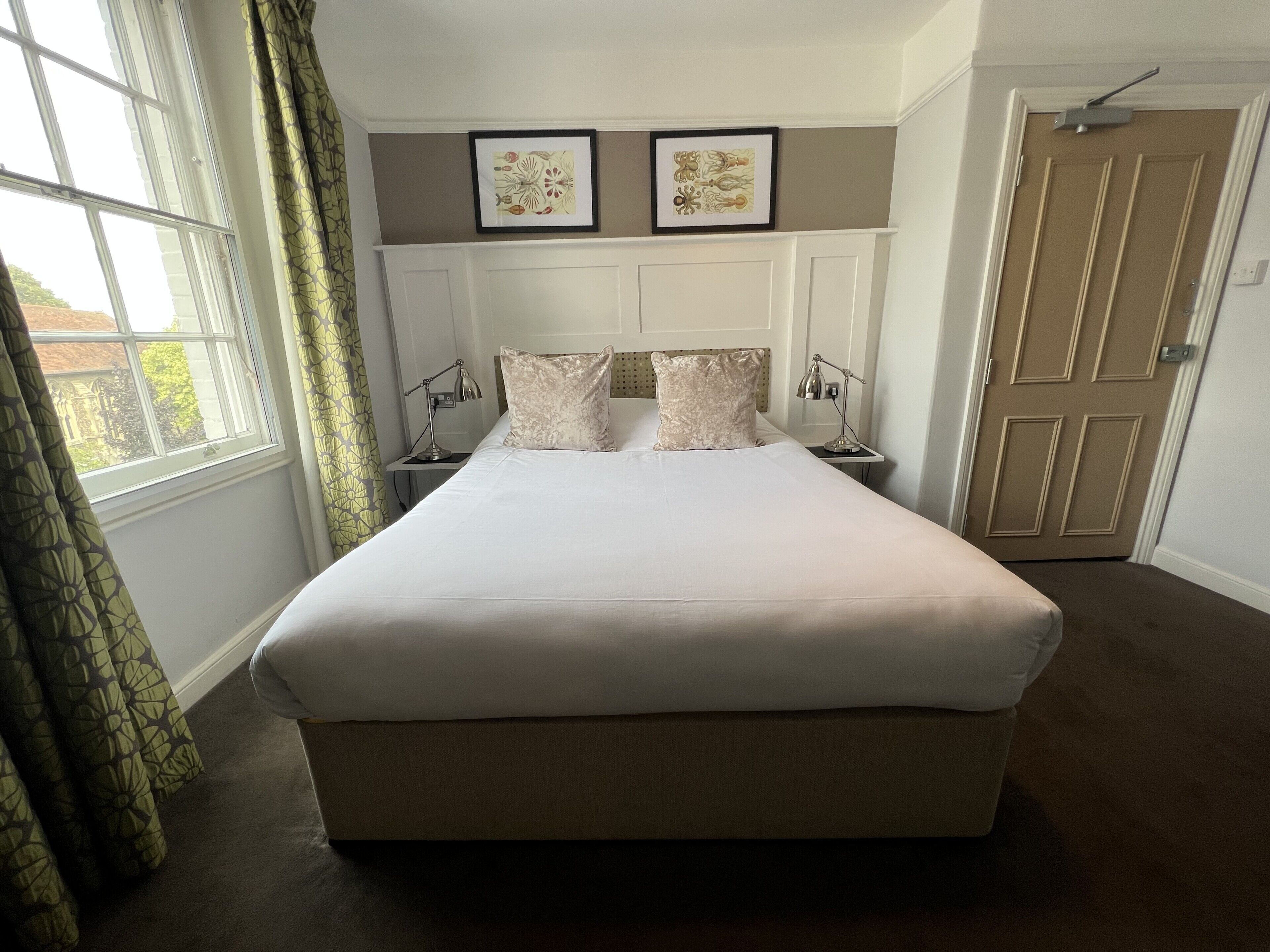 A neatly made bed with a headboard, two bedside lamps, and two framed pictures above the bed.