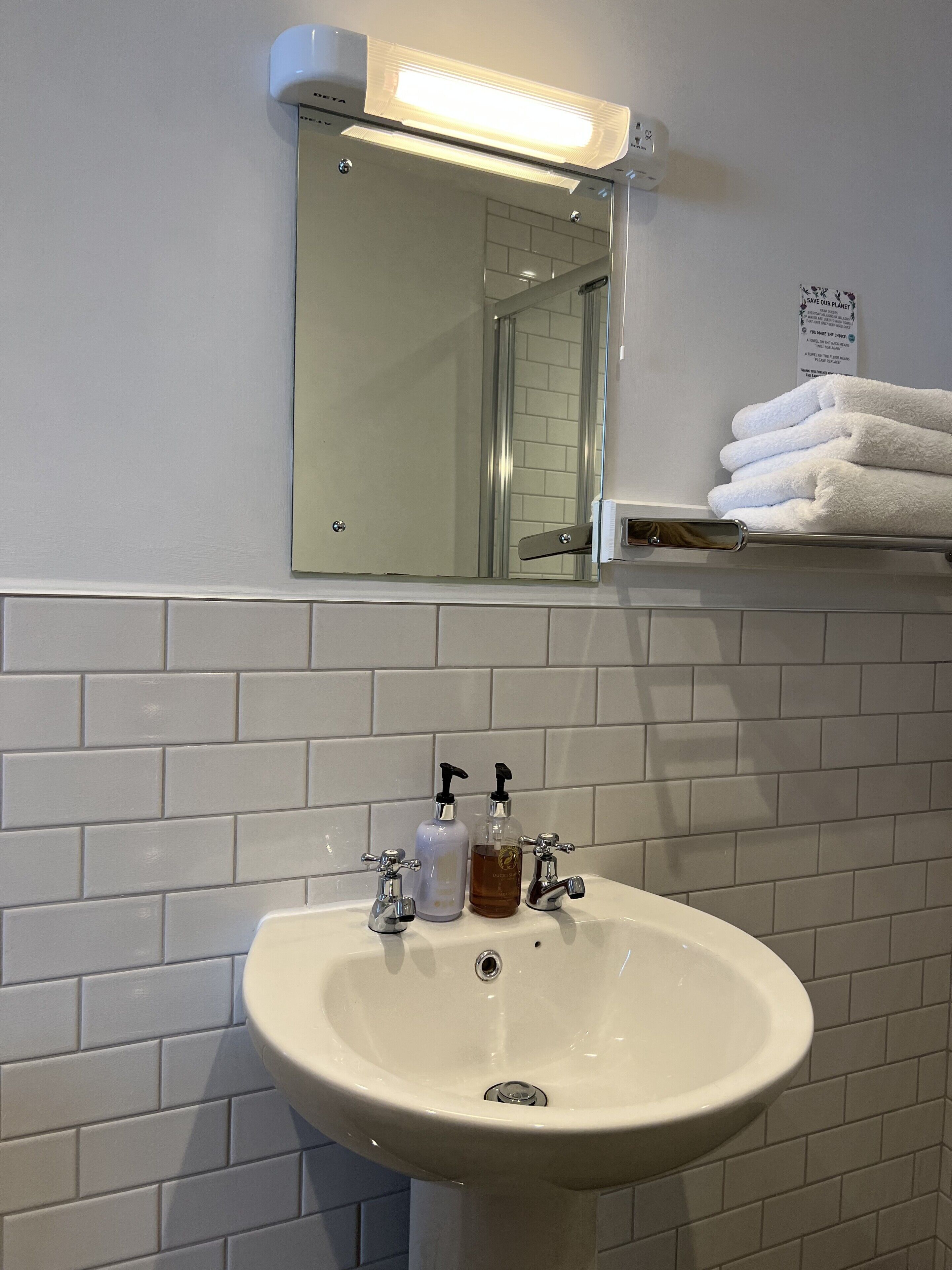 A bathroom with a white sink, two soap dispensers, a mirror, and a towel rack with folded towels.