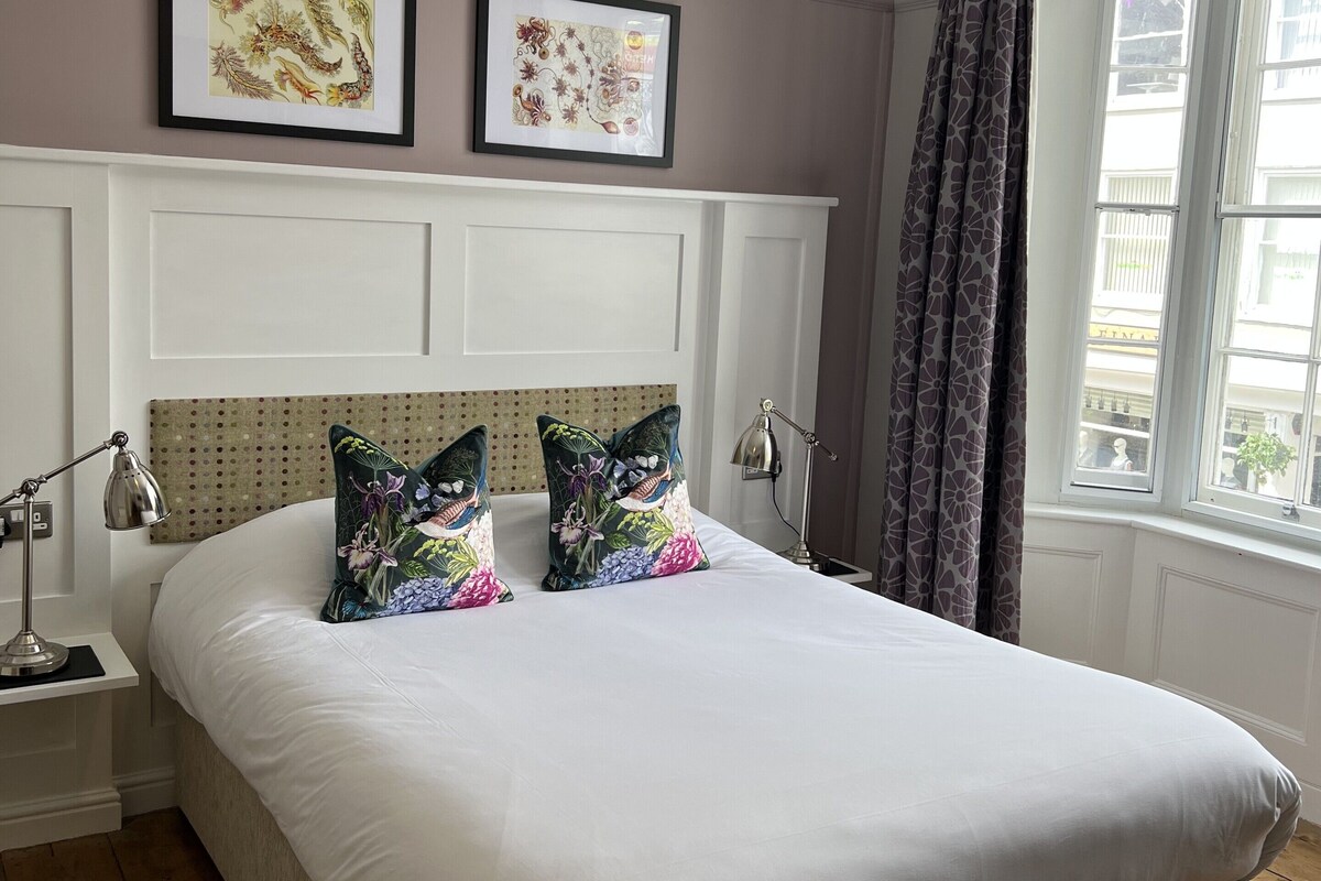 A neatly made bed with floral pillows, a white headboard, and a hanging light fixture.