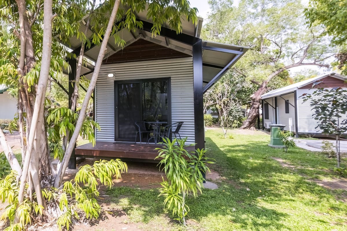 Una casa moderna con porche cubierto, un pequeño patio y un jardín con árboles y arbustos.