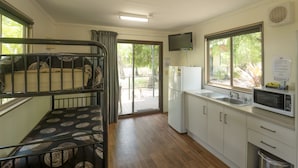 Cocina compacta con microondas, fregadero y refrigerador. Hay una pequeña zona de estar con un banco estampado y una puerta corrediza de vidrio que da a un balcón.