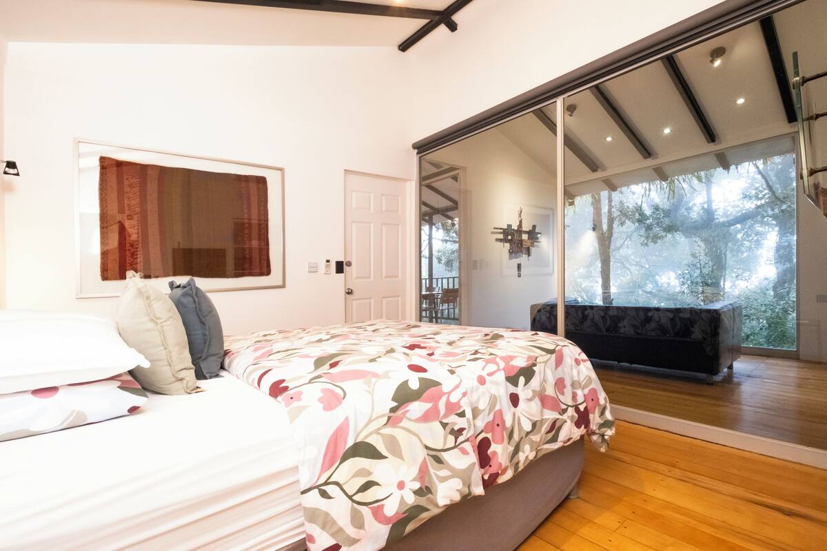 A bedroom with a large bed, a window, and a sliding glass door leading to a balcony.