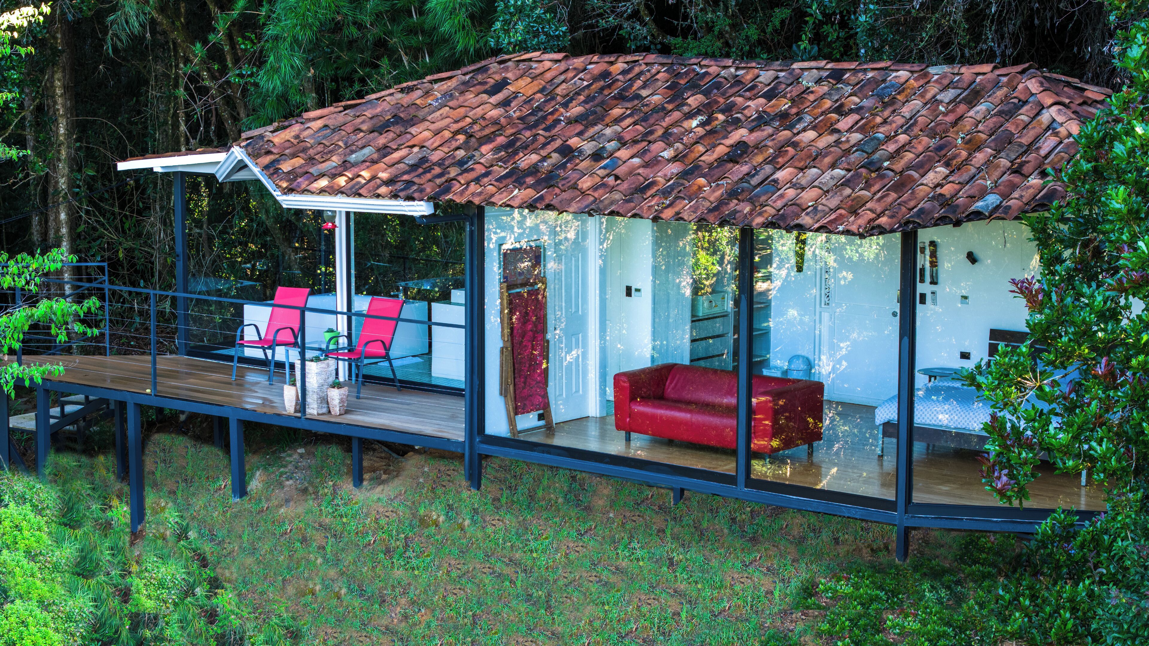 A modern house with a glass extension, red furniture, and a tiled roof.