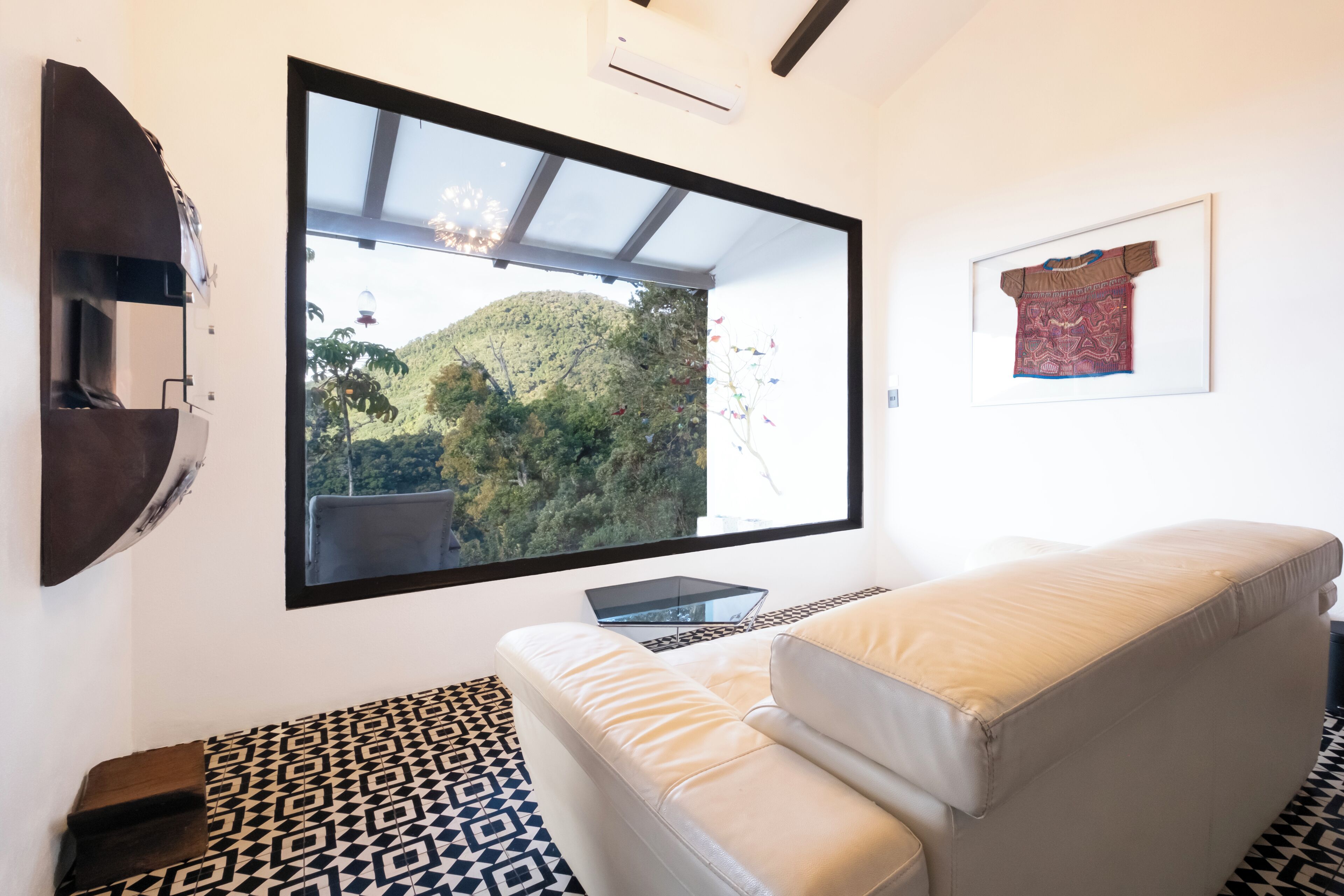 Ein modernes Wohnzimmer mit einem großen an der Wand montierten Fernseher, einer Couch, einem gemusterten Teppich und einem gerahmten Wandtextil.